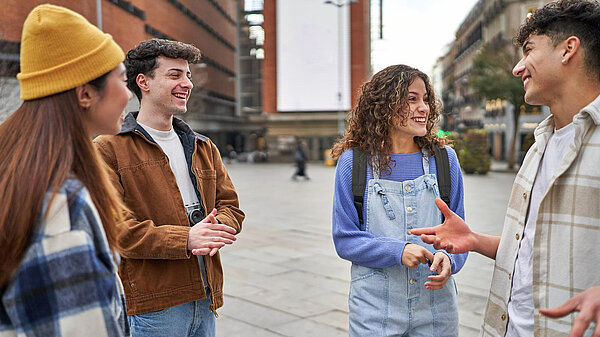 Four young people standing outside in a public square talking and laughing