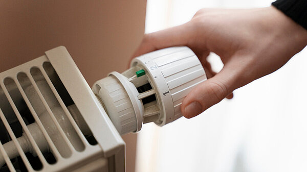 Close up of a hand turning the thermostatic valve on a radiator