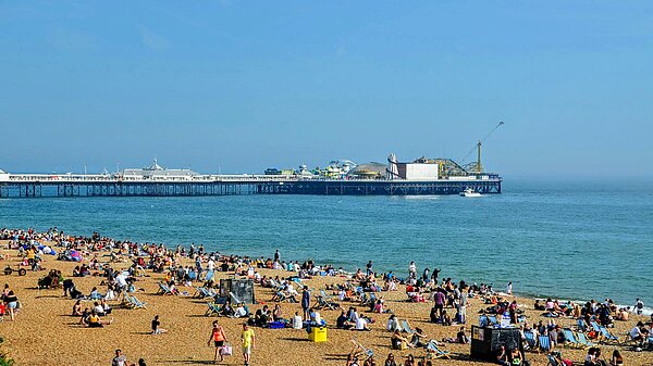 Brighton beach and pier. People are sat on the beach.