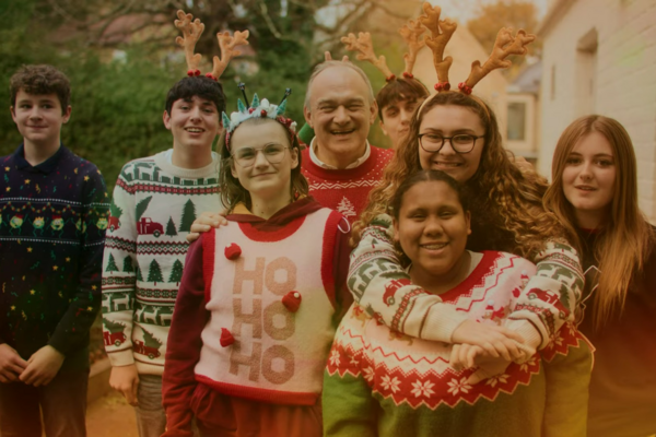 Ed Davey with young carers, everyone is dressed in Christmas jumpers and some people are wearing felt antlers on their head